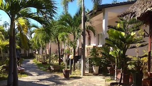 A pathway lined with potted plants and palm trees leading to a building with a thatched roof. - Suoi Tien Mui Ne Resort (Mui Ne)