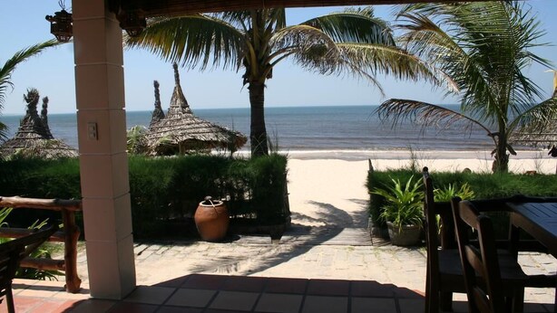 A beachside patio with a view of the ocean, palm trees, and thatched-roof structures. - Suoi Tien Mui Ne Resort (Mui Ne)