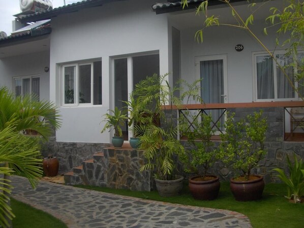 Una casa de dos plantas con una escalera de piedra que conduce a la entrada, rodeada de plantas en macetas y un pequeño jardín.