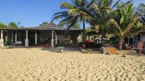 A beachside building with a covered patio area, palm trees, and a sandy beach. - Suoi Tien Mui Ne Resort (Mui Ne)