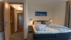Un dormitorio con cama, mesitas de noche, una puerta de madera, un cuadro en la pared y una cortina.