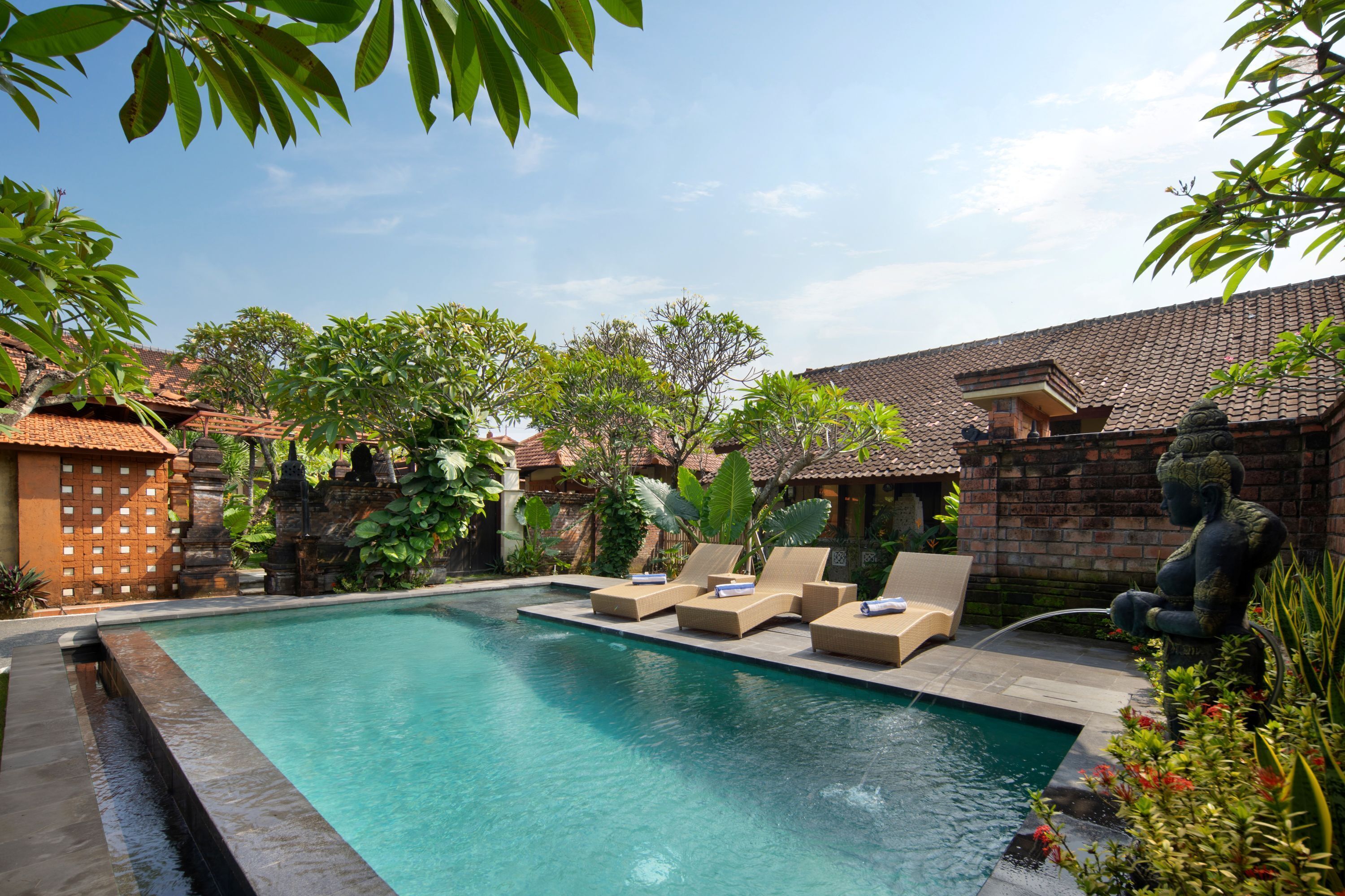 A swimming pool with lounge chairs, surrounded by greenery and traditional architecture.