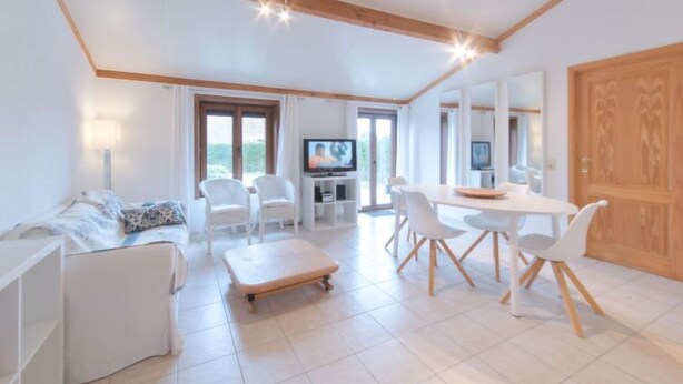 A spacious living area with a sofa, a dining table with chairs, a TV, and a wooden door. - Enjoy with parking by Interhome (De Haan)