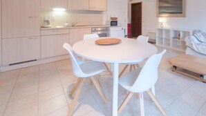 A modern kitchen with white cabinets, a round dining table with white chairs, and a wooden bench. - Enjoy with parking by Interhome (De Haan)