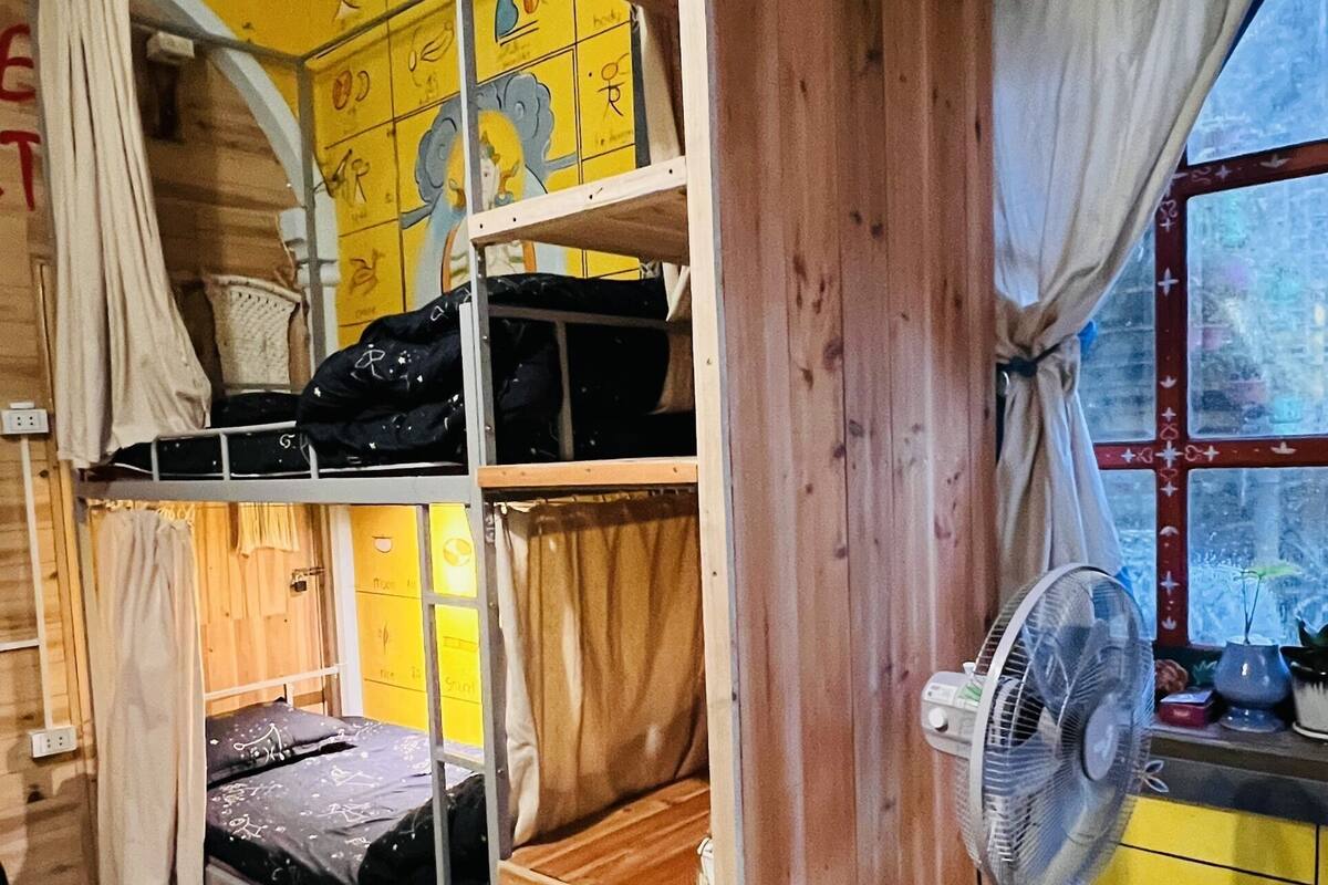 Ein Schlafsaalzimmer mit Etagenbetten, einem Ventilator und einem Fenster mit Vorhängen.