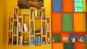 A room with a bookshelf filled with books and a camera, a colorful wall with a cityscape painting, and a door with a geometric pattern. - Saigonese Trekking House - Hostel (Sa Pa)