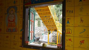 A window with a yellow staircase leading outside, a motorcycle parked outside, and a wall with various drawings and symbols. - Saigonese Trekking House - Hostel (Sa Pa)