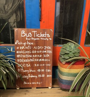 A wooden sign with bus ticket information for various pickup times and locations. - Saigonese Trekking House - Hostel (Sa Pa)