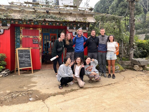 A group of people posing in front of a colorful building with a chalkboard sign advertising a trekking activity. - Saigonese Trekking House - Hostel (Sa Pa)