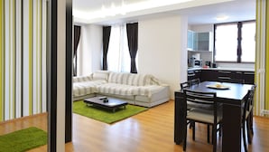 Ein modernes Wohnzimmer mit einer Eckcouch, einem Esstisch mit Stühlen und einer Küchenzeile mit Schränken und Geräten.