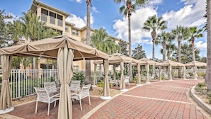 A resort patio with outdoor seating under umbrellas, palm trees, and a brick walkway. - Resort-Style Perks! Riverfront Gem in Palm Coast (Palm Coast)