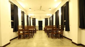 A hotel corridor with rows of wooden chairs and tables, a ceiling fan, and black curtains on the windows. - Sky 14 Hotel Apartments (Malabe)