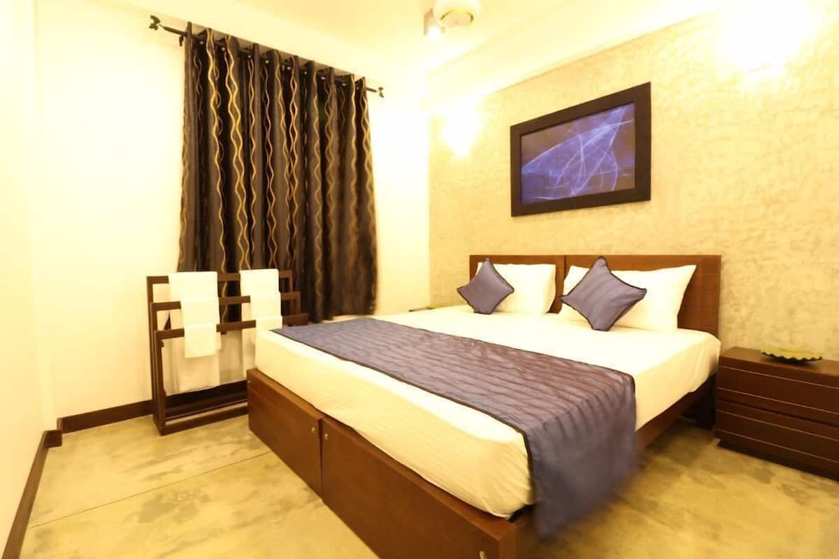Quarto de hotel com cama, mesa de cabeceira, televisão na parede e cortina.