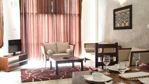 A hotel room with a dining area, a sofa, a TV, and a painting on the wall. - Sky 14 Hotel Apartments (Malabe)