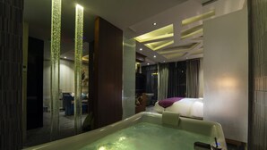 Una habitación de hotel moderna con una bañera grande, una cama con una colcha morada y un espejo que refleja la habitación.