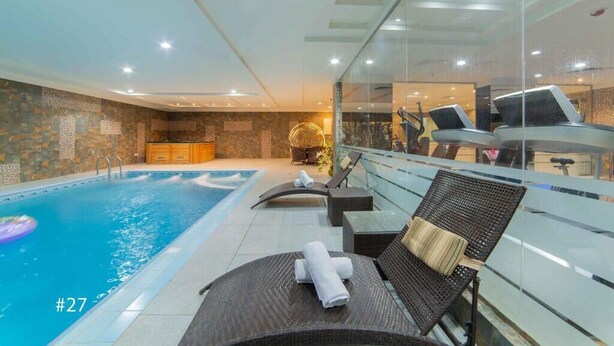 Un área interior de piscina moderna con sillones de descanso, una pared de vidrio y una pared de piedra.
