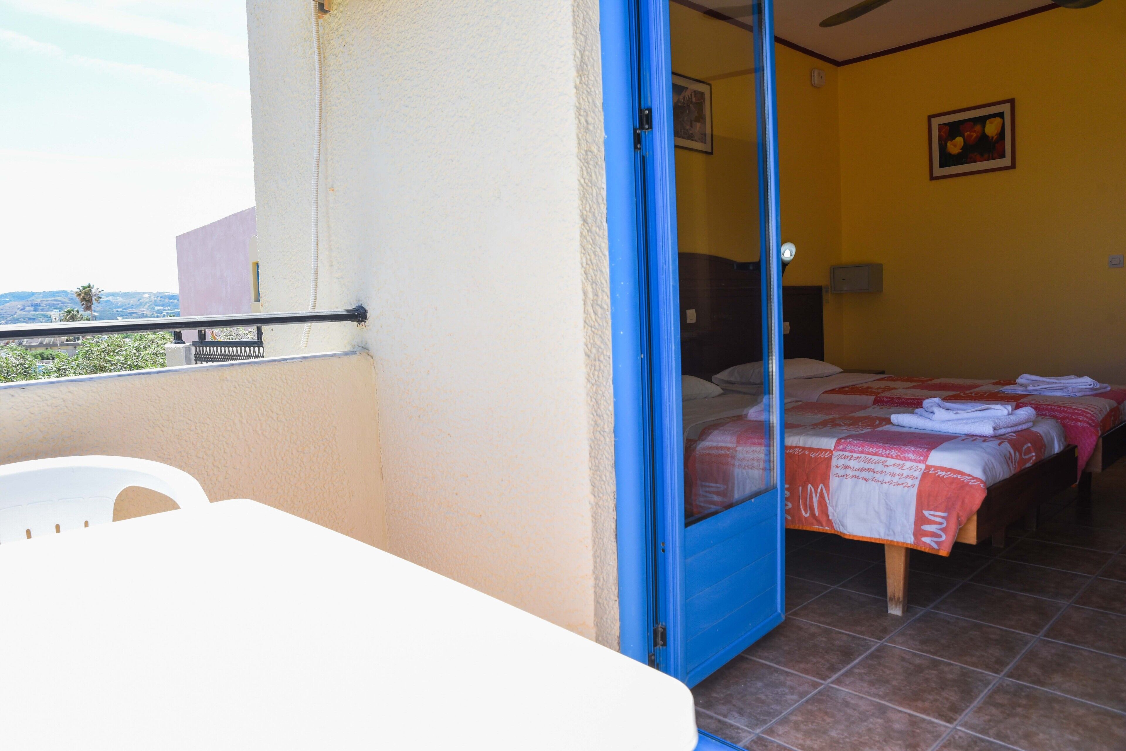 A room with a bed, a table, and a balcony.