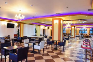 A spacious indoor area with multiple tables and chairs, a checkered floor, and decorative lighting.