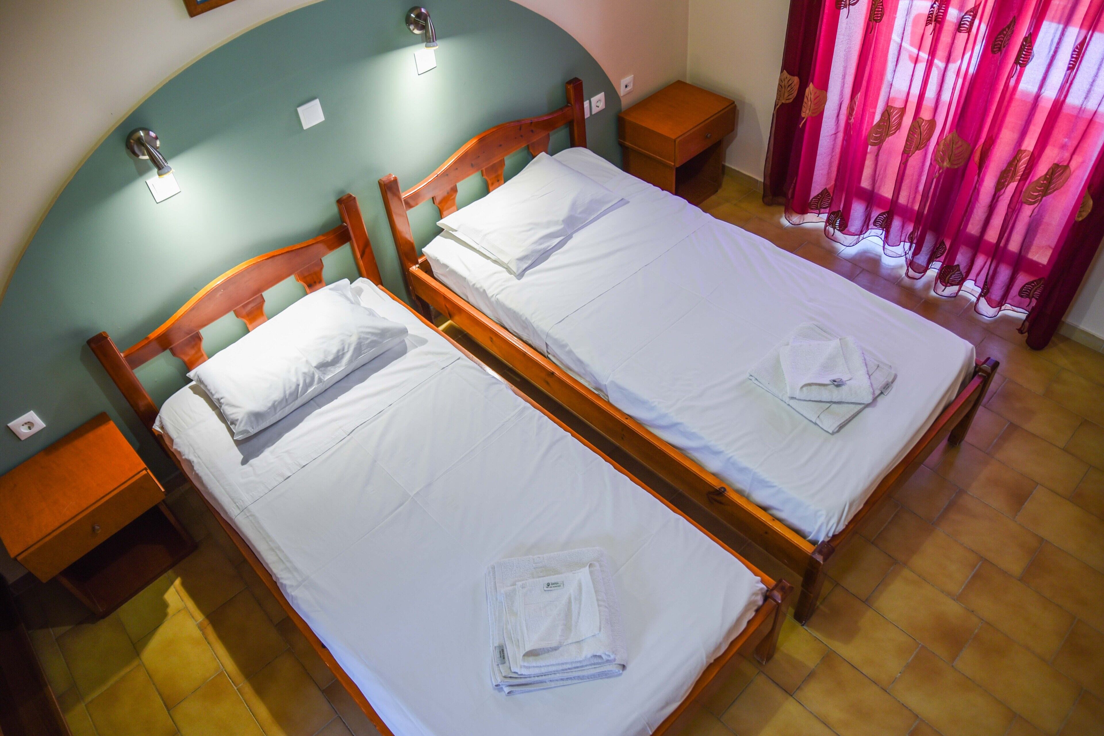 Two single beds with wooden headboards, white linens, and a small wooden nightstand with a drawer.