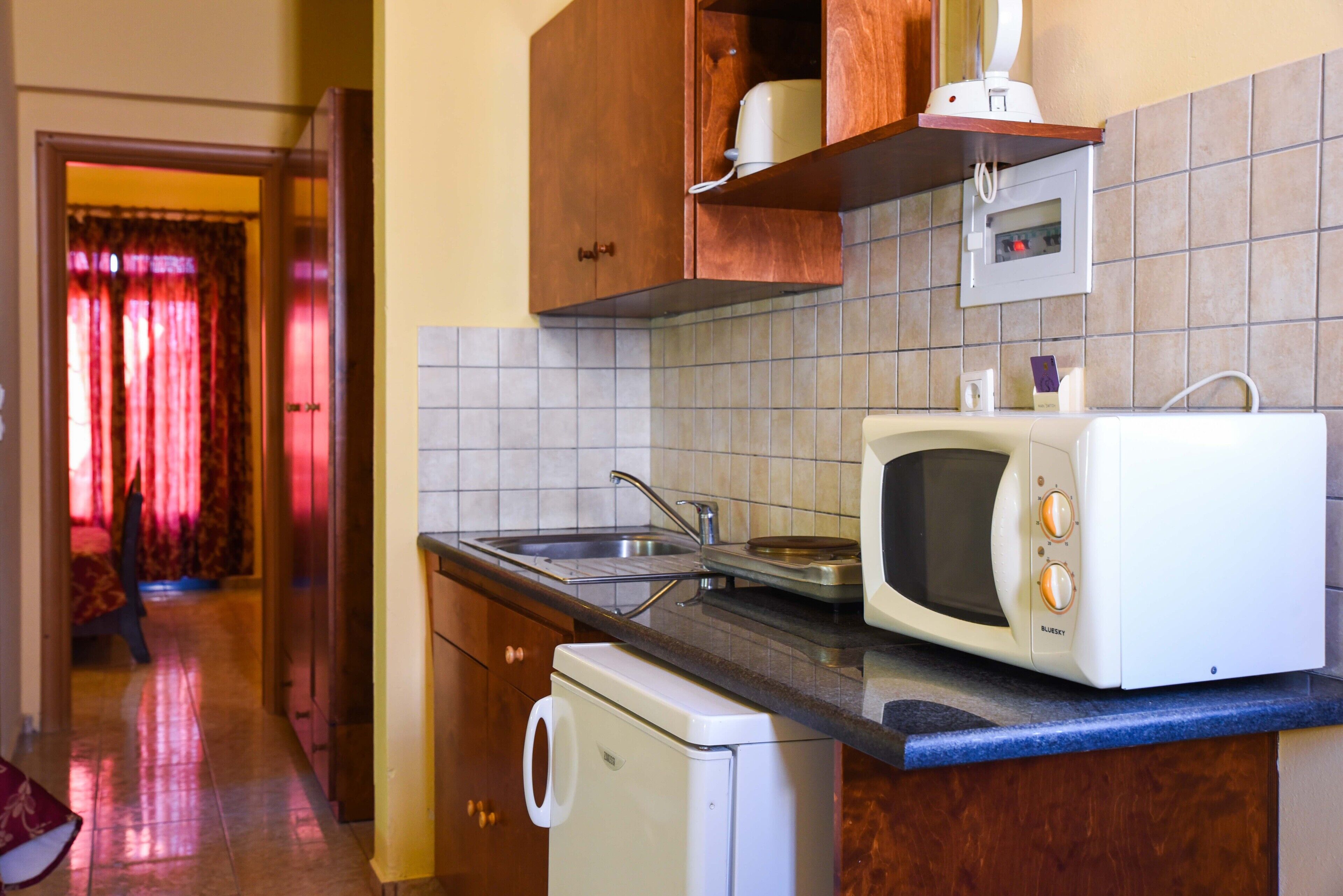 Una cocina con microondas, lavamanos y lavavajillas. Hay un armario de madera sobre el microondas y un salpicadero de azulejos.