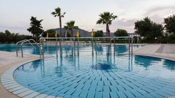 Una piscina con borde de azulejos, rodeada de palmeras y una montaña al fondo.