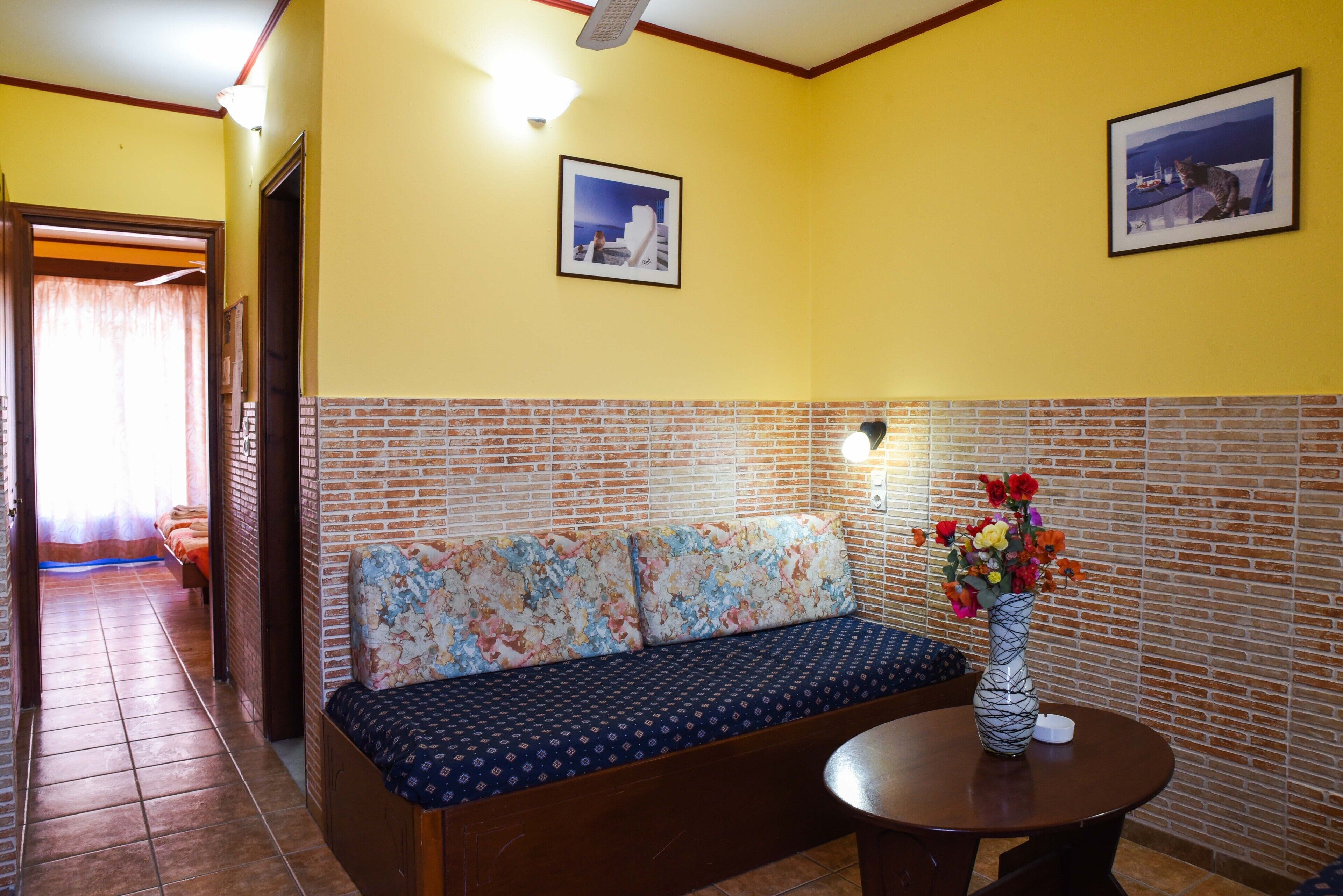 Una stanza con parete a mattoni, un divano con cuscino decorato, un tavolino con un vaso di fiori e due quadri appesi al muro.