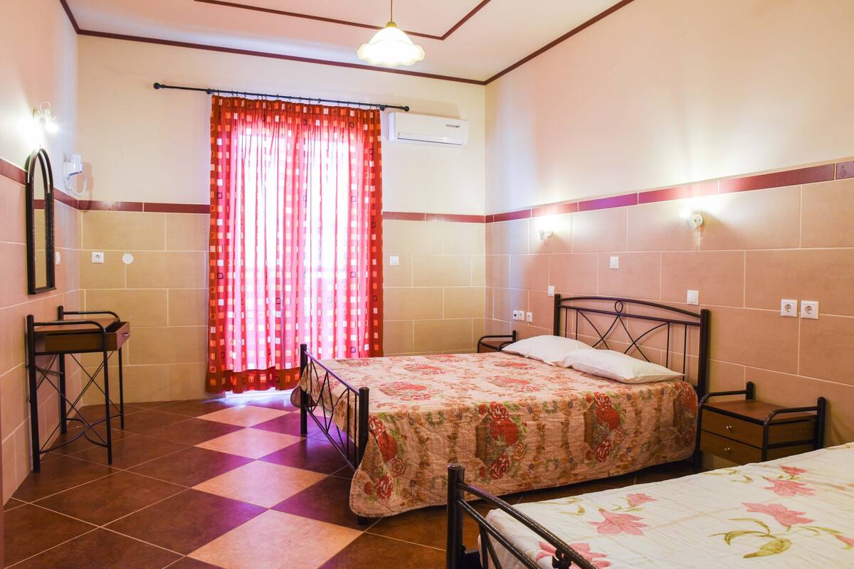 A bedroom with a bed, a small table, a mirror, and a window with curtains.