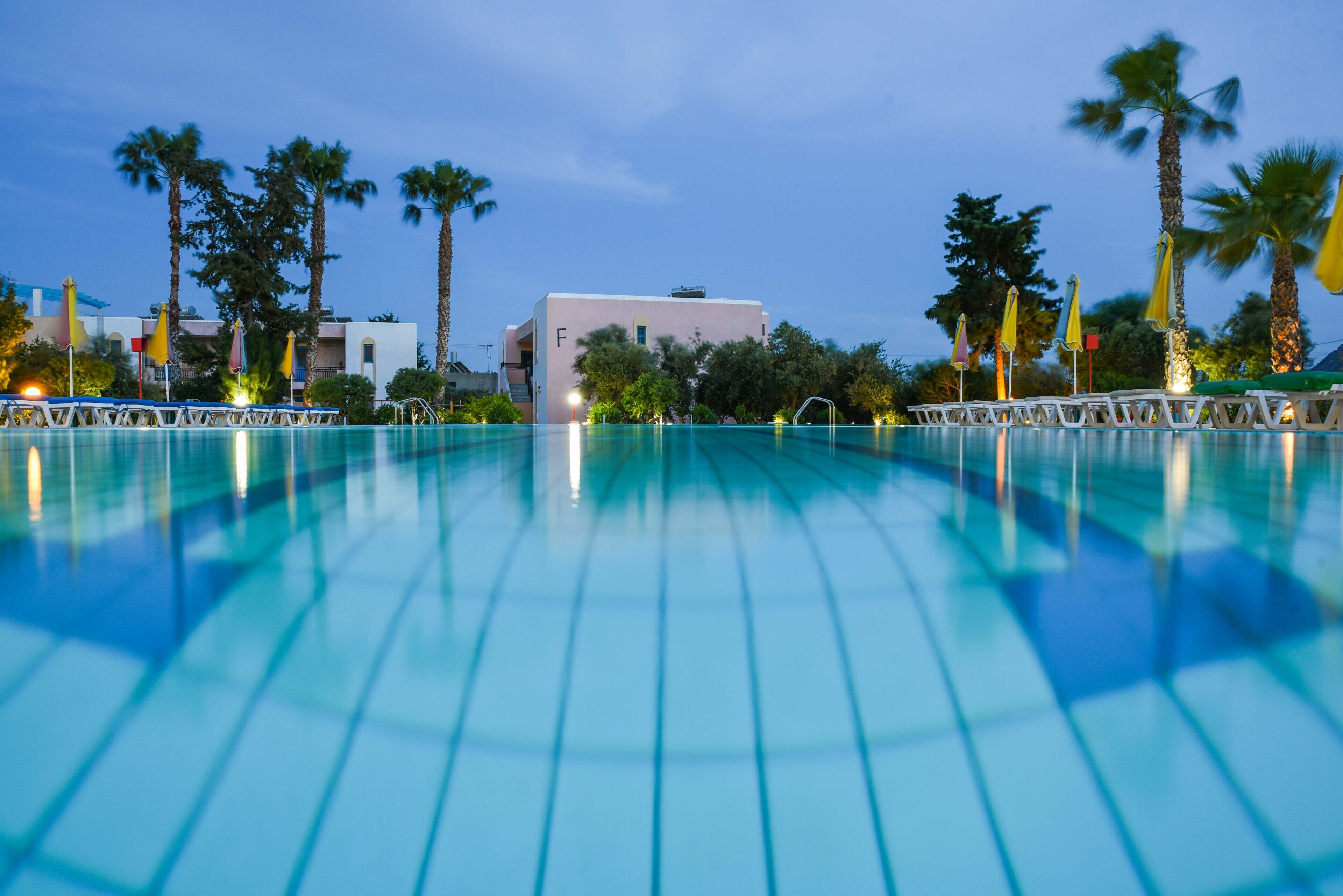 Ein Pool mit Blick auf ein Gebäude und Palmen im Hintergrund.