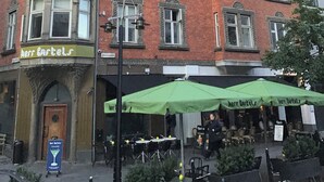 A corner building with a corner turret, multiple windows, and a green awning with outdoor seating.