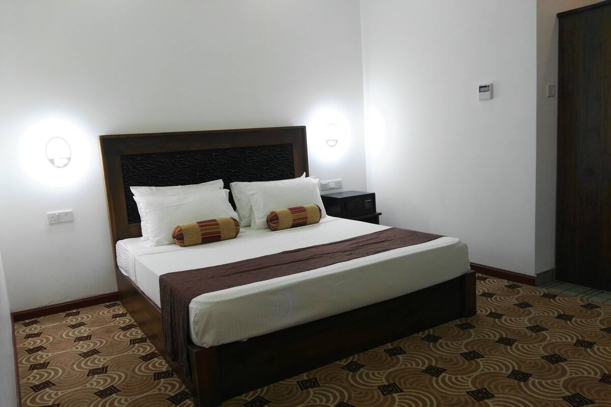 A neatly made bed with white linens and two decorative pillows, a dark headboard, and a patterned carpet.