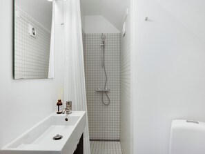 A bathroom with a white sink, mirror, shower, and tiled walls. - Saint - Nice 1-bdr Apt by the Canals (Copenhagen)