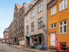 Una calle con edificios, un café con terraza y una bandera roja.