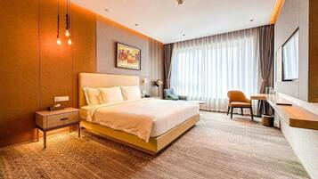 A hotel room with a large bed, bedside table, lamp, chair, and a view of the city through the window.