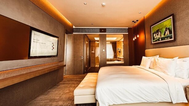 Una habitación de hotel moderna con una cama grande, una zona de estar, una pantalla de televisión y un cuadro enmarcado en la pared.
