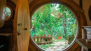 A room with a large circular window, a wooden surfboard leaning against the wall, and a hanging light fixture. - U Lesa Retreat Nha Ben Rung (Hanoi)