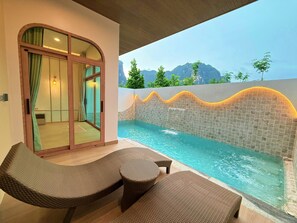 A pool area with a glass door leading to a room, wicker furniture, and a view of mountains.