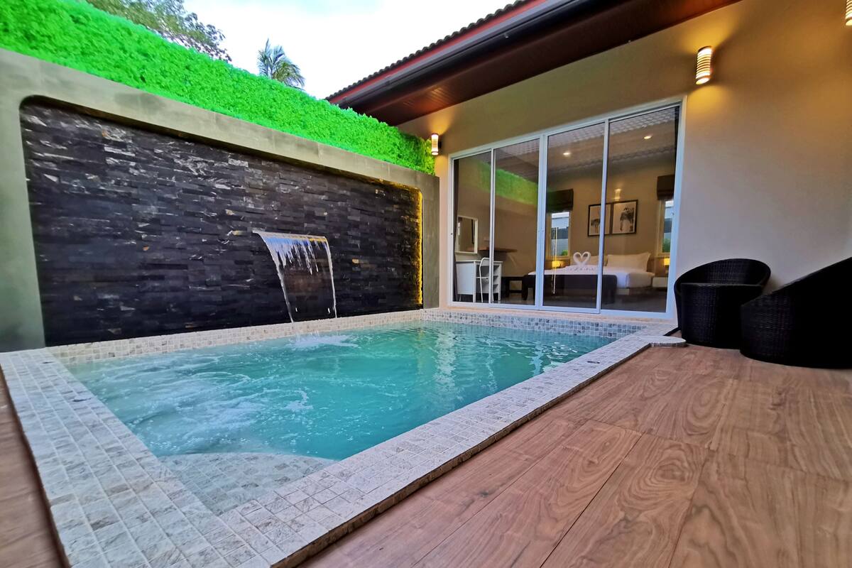 A swimming pool with a waterfall feature, surrounded by a wooden deck and a stone wall with a green vertical garden.