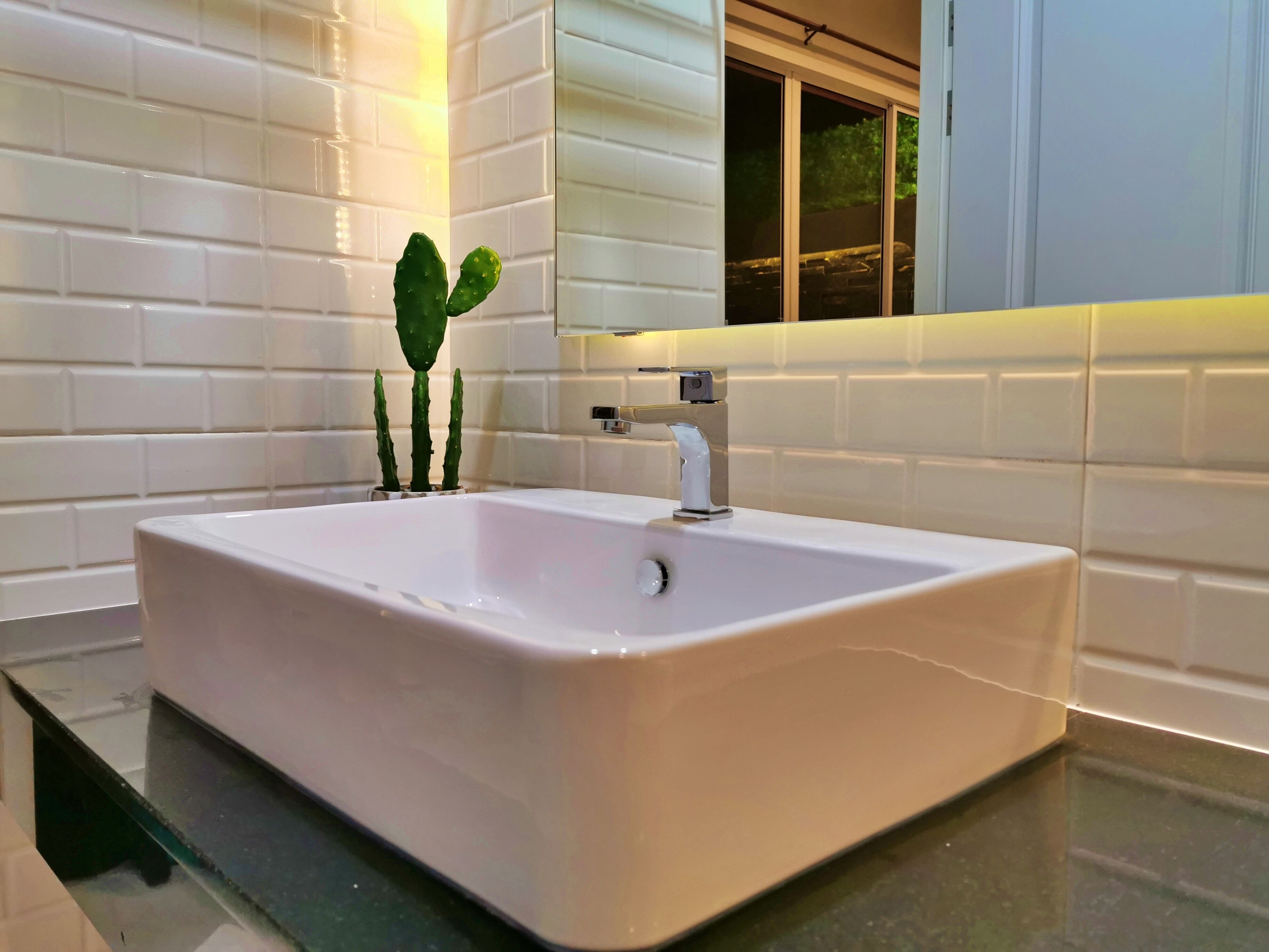 Lavabo blanco con grifo moderno, rodeado de baldosas blancas tipo metro.