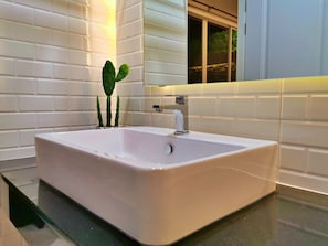 Un lavabo blanc dans une salle de bain, doté d’un robinet moderne, le tout entouré de carreaux de céramique blancs de style métro.