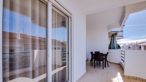 A balcony with a sliding glass door, a dining table with chairs, and a view of the cityscape.