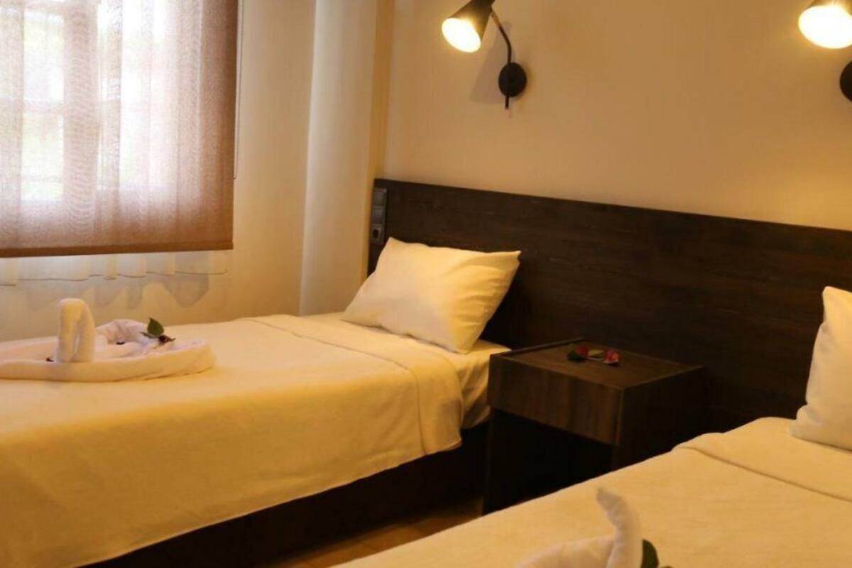 Une chambre d’hôtel avec deux lits, une tête de lit en bois, une table de chevet et une lampe fixée au mur.