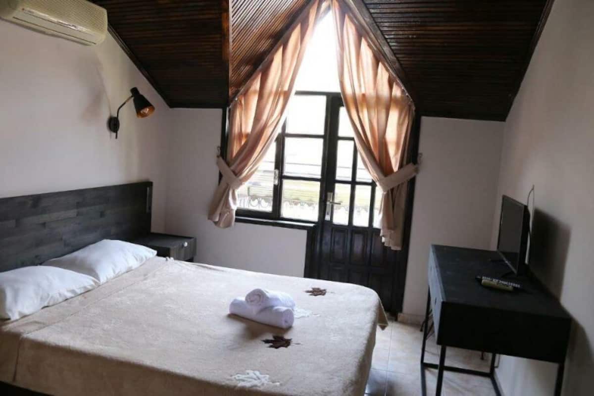 Une chambre à coucher avec un lit, un bureau, une télévision et une fenêtre avec des rideaux.