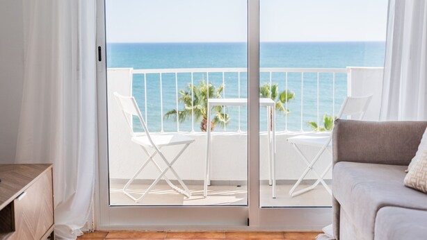 Un balcon avec vue sur la mer, une table blanche, deux chaises blanches et un canapé gris.
