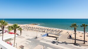 Un hôtel situé en bord de mer, offrant une vue sur l’océan, les palmiers et les parasols de plage.