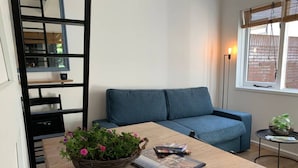 A cozy living room with a blue sofa, a wooden coffee table with a magazine and a basket of flowers, and a small side table with a plant.