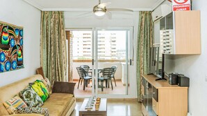 A living room with a sofa, a coffee table, a TV, and a balcony with chairs. - Lovely apartment for 6 people with A/C, pool, TV and terrace (Orpesa Oropesa Del Mar)