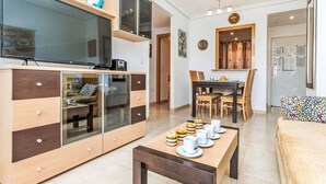 A modern living room with a flat-screen TV, a wooden cabinet with glass doors, a dining area with a wooden table and chairs, and a cozy sofa. - Lovely apartment for 6 people with A/C, pool, TV and terrace (Orpesa Oropesa Del Mar)