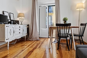 A room with a wooden floor, a white dresser, a dining table with chairs, and a potted plant.