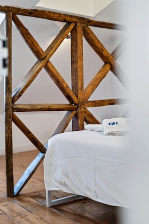A bed with a white sheet and a folded towel, a wooden trestle structure, and a wooden floor. - Camões Cool Loft, at Chiado (Lisbon)