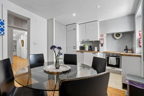 A modern kitchen with a dining area, featuring a glass table, chairs, and a vase with flowers. - Camões Cool Loft, at Chiado (Lisbon)